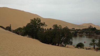 Huacachina oasis in huge sand Peruvian dunes, green trees, water lake in desert..