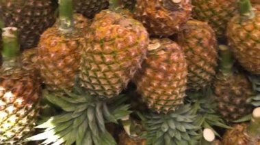 Many ripe pineapples laying in pile, hand points on the pineapple, fruit market...