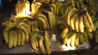 Many yellow bananas fill frame, pile of bananas captured in light sold in market.