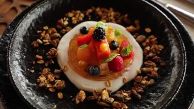 Beautiful appetizing dessert of berries on a jelly with milky sauce and nuts in black plate