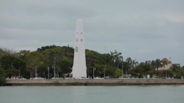 Caribbean embankment cars parked between palm trees huge white stella lighthouse..