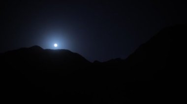 Spooky bright small moon in complete darkness over the big black mountain ..