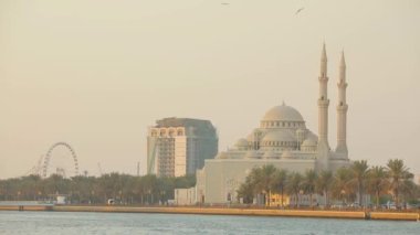Arabic town with huge mosque and hotel with palms near water in Sharjah city..