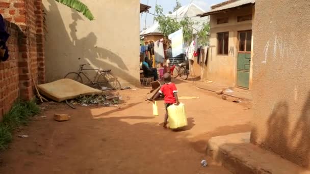 Mały Afrykanin Chodzi Slumsach Niosąc Duże Pojemniki Obu Rękach — Wideo stockowe