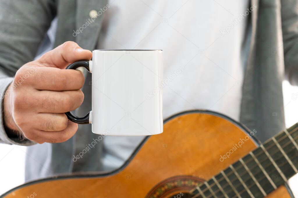Close-up male hand with a mug of drink. Standard 11oz white ceramic mug with black handle with copy space for your design. Musician hold gitara and drink cofe