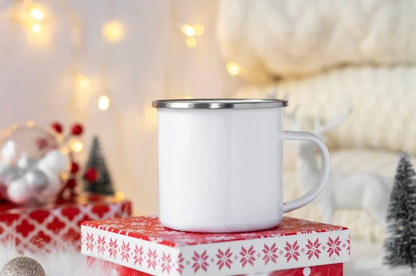 Burla de moda para la marca de la taza de camping de esmalte blanco con anillo de acero inoxidable de pie sobre la caja de Navidad. Fondo de decoración de Navidad. Copiar espacio para su diseño Imagen de archivo