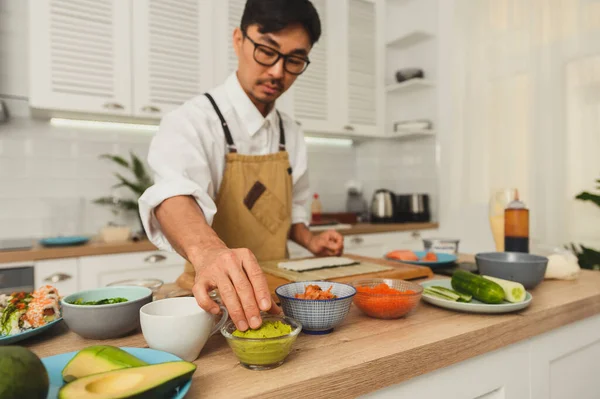 Asiatischer Meister bereitet Sushi in der Küche zu. Mann steht in der Küche und nimmt Sushi-Zutaten auf den Tisch. Gesundes Essen naschen Konzept im Restaurant. Konzept zur Lieferung frischer Lebensmittel — Stockfoto