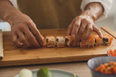 Suşi ustaları elleri yakın çekim. Erkek bir şef suşi yapar ve pirinç, kırmızı balık ve ahşap tabakta avokado yapar. Taze yemek servisi. 