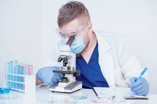 Virologista olhando em um microscópio em vidro de teste com sangue em laboratório. Conceito de análise ao sangue — Fotografia de Stock