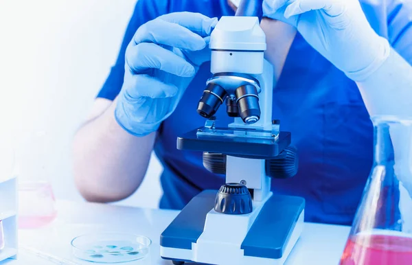 Close-up virologista olhando em um microscópio de vidro com amostra de sangue em laboratório. Conceito de análise ao sangue — Fotografia de Stock