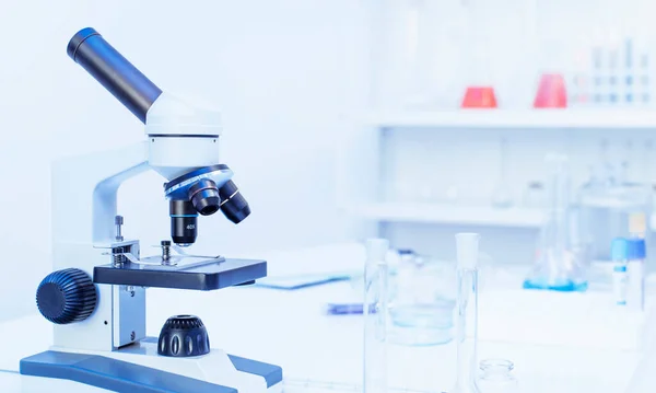 Vidros de laboratório com líquidos coloridos e microscópio sem ninguém. Teste de DNA, sangue e conceito de testes COVID-19 — Fotografia de Stock