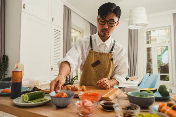 Asiatische Sushi-Meister machen Sushi-Rollen auf einem Küchenhintergrund. Zutaten für Sushi auf dem Tisch — Stockfoto