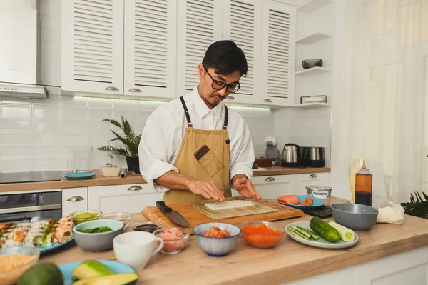 Stillleben Porträt des Chefs beim Zubereiten von Sushi. Asiatische Meister tragen Uniform und legen Reis für Sushi auf einen Teller. Umgeben von Zutaten für die Herstellung von Sushi — Stockfoto