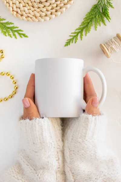 Acercamiento Cug café blanco burla. Manos femeninas sostiene taza de cerámica. Piso tendido bordeado conramas de abeto y decoraciones de Navidad — Foto de Stock