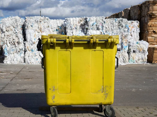 Ön plandaki sarı çöp tenekesinin yanında büyük miktarda atık kağıdın fotoğrafı..