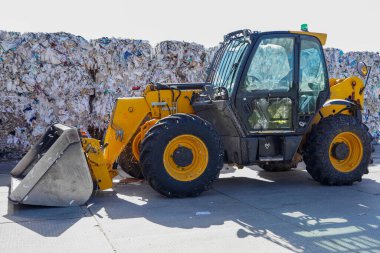 Çöplüğün arka planında sarı bir traktörün fotoğrafı..