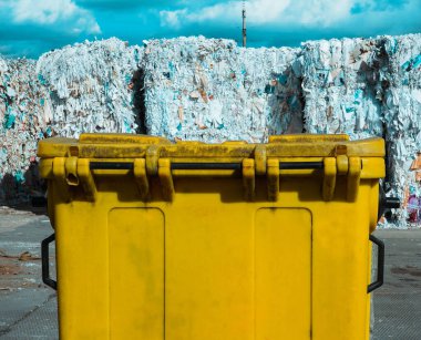 Ön plandaki sarı çöp tenekesinin yanında büyük miktarda atık kağıdın fotoğrafı..