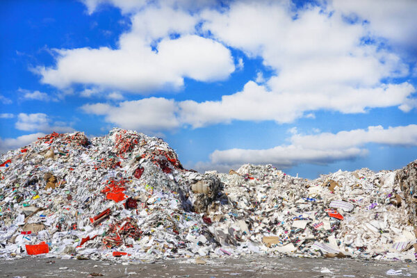 Фото большого количества мусора и мусора на свалке на улице под голубым небом с белыми облаками.