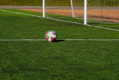 Futbol sahasının yeşil çimenliğindeki topun fotoğrafı caddedeki kapının yanında..