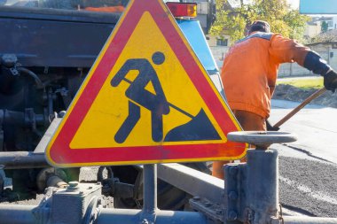 Yol çalışmalarının arka planında kırmızı-sarı üçgen yol tabelası..