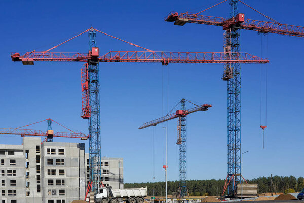 The process of building a gray house next to cranes and construction machinery on the street.