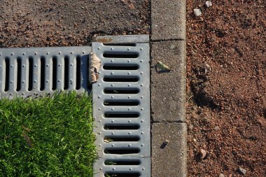 Yeşil çimenlerin, kumun, su kanalının ve sokaktaki sınırın fotoğrafı.