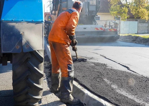 Turuncu tulumlu, asfalt döşeyen bir adamın fotoğrafı..
