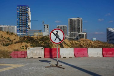 Şehirdeki çok katlı binaların arka planında üstü çizili bir adamla yuvarlak beyaz yol tabelası..