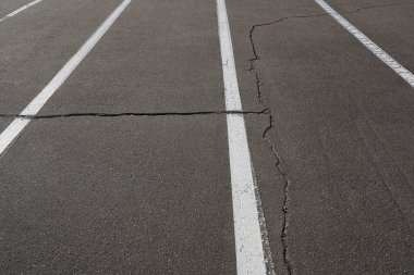 Üzerinde çatlaklar ve beyaz işaretler olan gri asfalt yolun fotoğrafı..