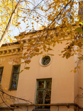 Ağaçların ve gökyüzünün yakınında sarı bir evin penceresi olan eski açık bir balkonun dikey fotoğrafı..