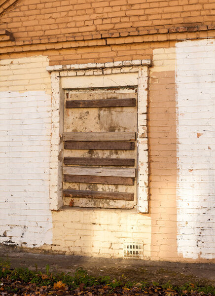 Photo of a boarded up window of a brick house on the street.