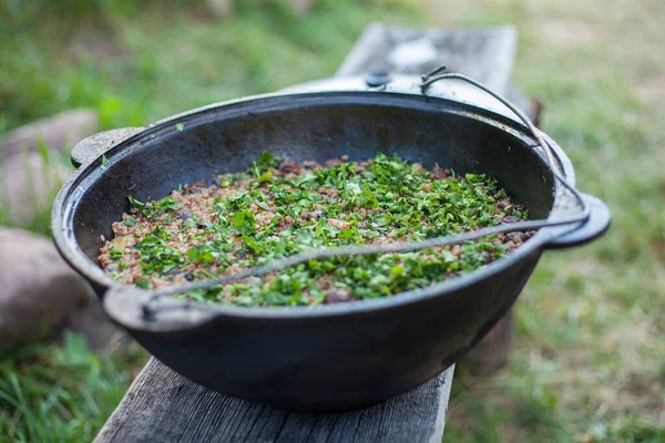 Doğada bir kazanda bitkilerle karabuğday pişirme sürecinin fotoğrafı..
