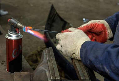 İşçi, yeni ve özel bir şekil yaratmak için metal bir aleti gaz tabancasıyla ısıtıyor..