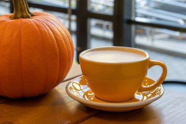 Bir fincan sarı fincanda çay tabağında bir fincan kahve ve ahşap bir masada turuncu bir balkabağı. Sonbahar. Kafe kavramı.