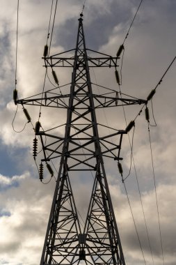Mavi gökyüzüne karşı beyaz bulutlu elektrik kabloları olan direklerin dikey fotoğrafı..