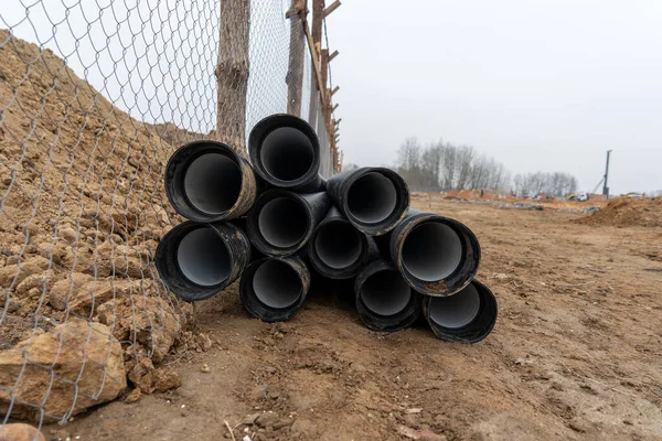 Metal bir çitin yakınındaki bir inşaat alanındaki siyah boruların fotoğrafı..