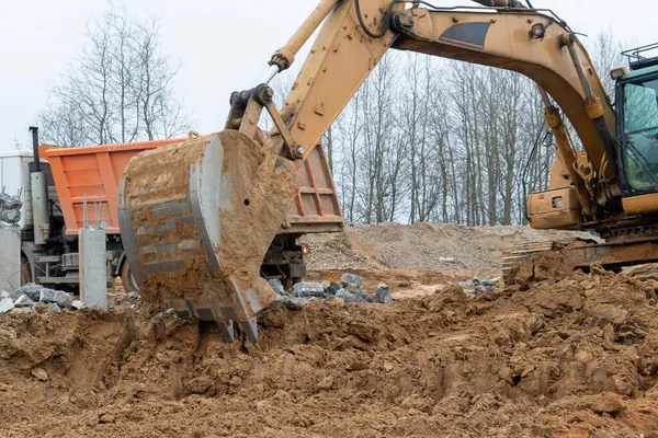 Sarı bir kazıcı ve turuncu bir kamyonun sokakta bir şantiyede çekilmiş fotoğrafı..