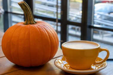 Bir fincan sarı fincanda çay tabağında bir fincan kahve ve ahşap bir masada turuncu bir balkabağı. Sonbahar. Kafe kavramı.