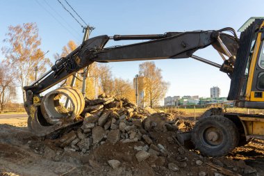 Ağaçların arkasındaki inşaat alanında zemin kazan sarı çamurlu bir kazıcının fotoğrafı. Yapısal bir kavram. İnşa ediliyor.