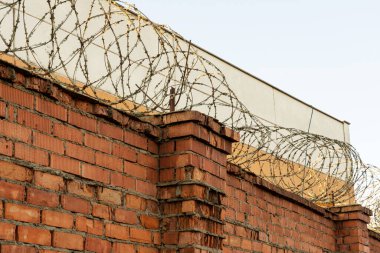 Dikenli telli kırmızı tuğlalı bir duvarın fotoğrafı. Eskrim ve çit.