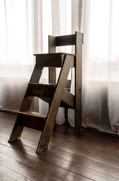 Beyaz perdelerin arka planına karşı küçük tahta bir merdivenin dikey görüntüsü. Fotoğraf stüdyosu.