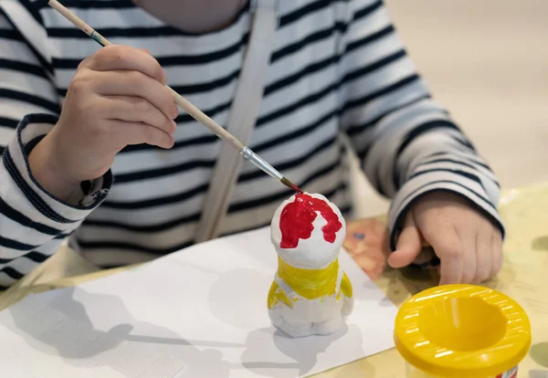 Bir kızın fotoğrafı kilden bir oyuncağı fırçayla boyuyor..