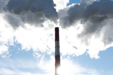 Mavi gökyüzüne karşı termik santralin tüten boruları. Büyük mavi boru beyaz buhar çıkarır. Kirletici bir fabrikanın bacaları..