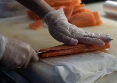 Eldivenli güzel manikürlü kadın elleri kırmızı bir balığı kesiyor.