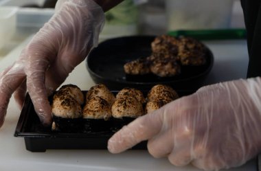 Bir şefin elleri hazır rulo ekmeği kutudaki balıklarla birlikte paketliyor.