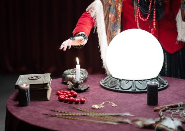 Kadın astrolog elini mumların üzerinde tutuyor. Astroloji için malzemeler masada. Yanan mum ve kristal küre.