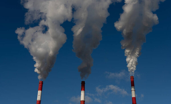 thick smoke from white-red pipes against a blue sky. 