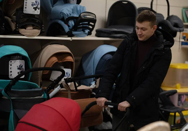 Gelecekteki bebeği için bebek arabası seçen genç bir babanın fotoğrafı. Güçlü dost aile.