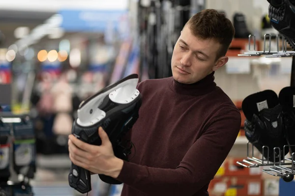 Genç adam spor bölümünde paten seçiyor. Bıçağın keskinliğini gözleriyle kontrol ediyor.