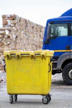 Arka planda bir çöp kutusunun fotoğrafı çöp arabası ve karton balyalar.